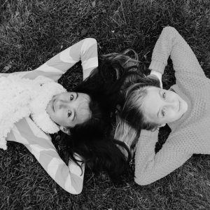 Two young girls lying on the grass with their hand behind their heads, smiling to the camera